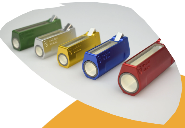 Five metallic cylindrical flashlight batteries in green, silver, gold, blue, and red, arranged diagonally on a white surface with a curved orange accent shape.
